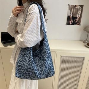 Sac fourre-tout minimaliste en toile léopard bleu porté à l'épaule dans un décor moderne