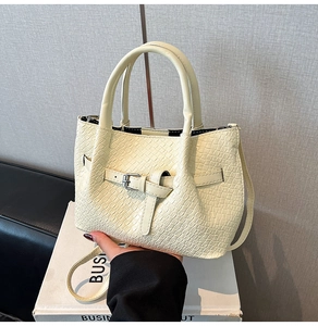 Detailed macro view of the cream woven texture and metal buckle on the leather handbag