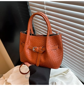Detailed view of an orange woven leather handbag with metallic buckle and sturdy top handles