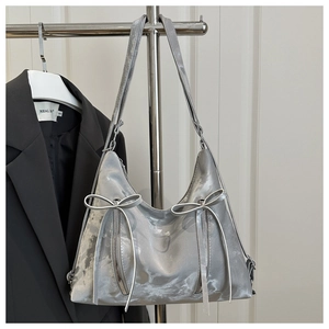 Detail of silver metallic hobo bag featuring two decorative bows and vertical zippers
