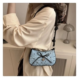 Close-up of light blue pleated leather bag featuring black bows and a heart pendant