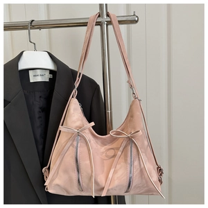 Detail view of pink suede shoulder bag with ribbon bow and parallel metal zippers