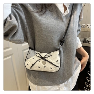 Detail of white bow-print crescent bag with silver heart pendant and pleated texture