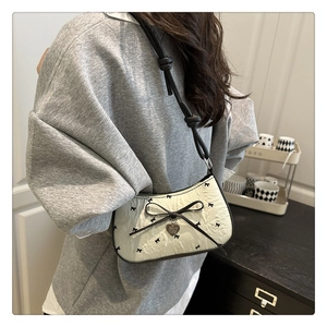 Chic cream crescent shoulder bag with black bows and heart charm worn by a model