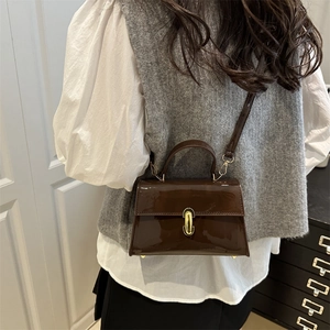 Sac baguette en cuir verni marron avec boucle dorée, porté par un mannequin chic