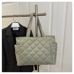 Detail of light green quilted tote bag with side pocket hanging on a metal rack