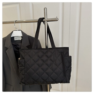Detail of black quilted tote bag with diamond pattern and functional side pocket