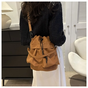 Detail van een bruine bucketbag met trekkoord gedragen door een model in een interieur