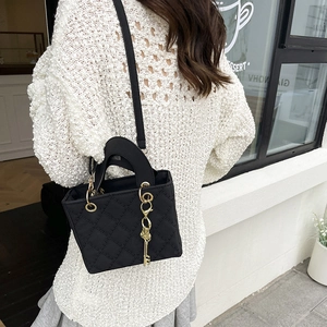 Quilted black nylon crossbody bag with gold chain and key charm in outdoor setting