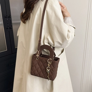 Brown quilted leather crossbody bag with gold key charm and top handle on model