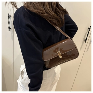 Detail of dark brown patent leather shoulder bag with elegant gold metallic buckle