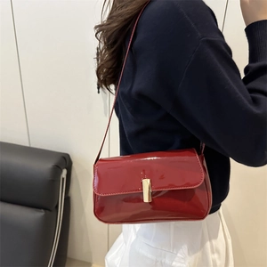 Chic retro red glossy patent leather shoulder bag with a gold buckle worn by a model
