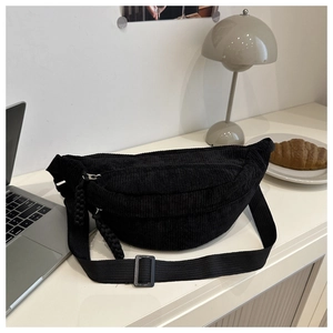 Vue détaillée du sac croissant en velours côtelé noir avec bandoulière sur un bureau chic