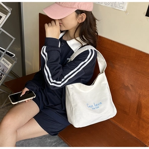 Detail of cream canvas tote bag with blue script and half-moon shoulder strap design