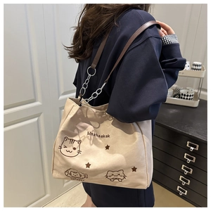 Detail of canvas tote bag with embroidered cat motif and leather strap with silver chain
