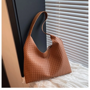 Detailed view of brown woven leather tote bag placed on elegant white fabric background
