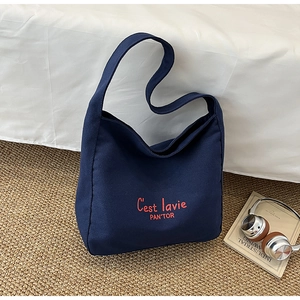 Detail of navy blue canvas tote bag with orange lettering and minimalist literary aesthetic