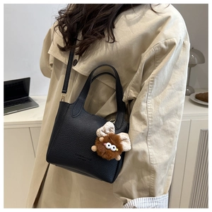 Detail of black lychee grain leather bucket bag with cute furry monster charm and gold hardware
