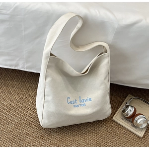 Detail view of beige canvas tote bag with artistic blue C'est lavie text printing