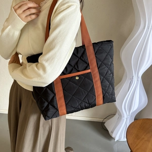Black quilted tote bag with brown straps and diamond pattern shown on a female model