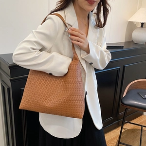 Chic brown woven tote bag with leather strap shown on shoulder in a cozy indoor setting