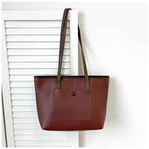 Gros plan détaillé d'un sac cabas en cuir marron-rouge foncé avec texture grainée et poche