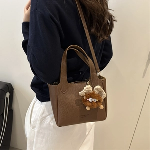 Brown lychee leather handbag with shoulder strap and plush monster charm decoration