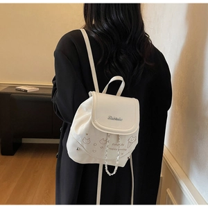 Detail of a creamy white leather backpack with cat embroidery and chain drawstring on a model