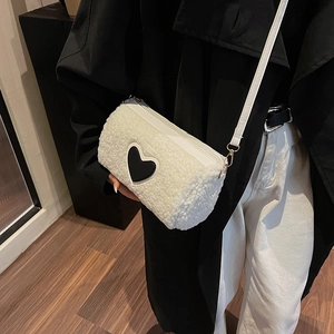 Sac cylindre minimaliste en peluche blanche avec patch cœur noir porté par un mannequin