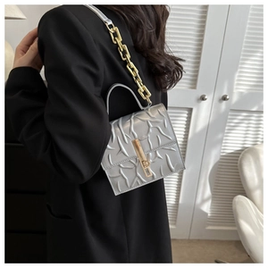 Detail view of silver embossed branch texture and gold chain strap on the handbag