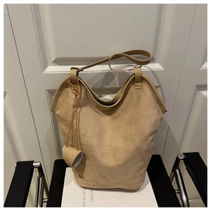 Detail view of beige suede tote bag with smooth leather trim on black designer chair