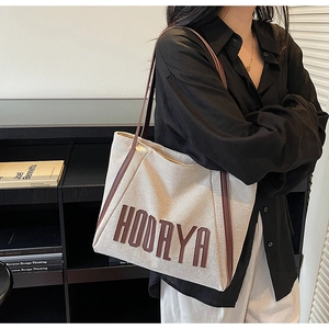 Detail view of canvas tote bag featuring brown leather trim and HOORYA letter print