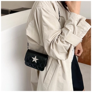 Detail of a black quilted mini crossbody bag with a silver diamond star and metal chain