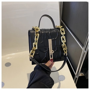 Detail of the black textured handbag with golden rectangle lock and chain strap