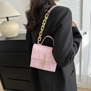 Pink crossbody bag with embossed texture and gold chain strap worn by a model
