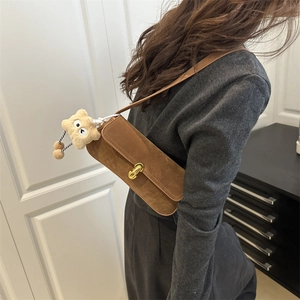 Brown suede baguette shoulder bag with gold clasp and star charm worn by a model