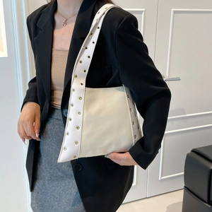 Sac sous le bras chic clouté en similicuir crème porté avec un blazer noir chic
