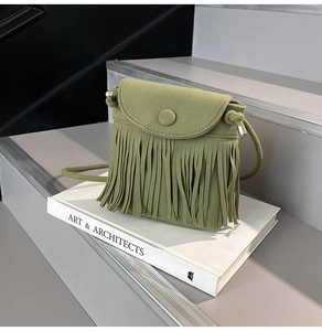 Detail of olive green suede tassel bag with fringe and round buckle on a book