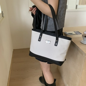 Chic white woven tote bag with black leather trim and silver rivets for elegant commuting