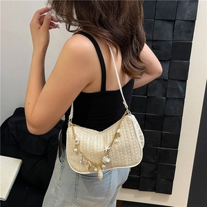 Straw woven shoulder bag with pearl shell charms shown on model in natural cream