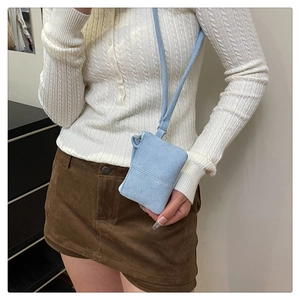 Hellblaue minimalistische Umhängetasche getragen von Modell mit weißem Strickpullover