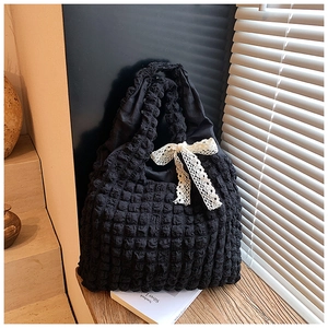 Detail of black popcorn fabric tote bag with lace bow on a white notebook and wood ledge