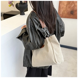 Detail of corduroy tote bag featuring brown leather strap and metal chain connection