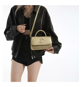 Close-up of golden metallic handbag with M logo buckle and adjustable strap
