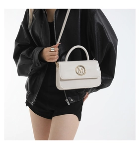 Close-up of a stylish cream leather crossbody bag with a golden M metal buckle