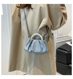 Detail of light blue pleated cloud bag with white pearl handle and glossy leather finish