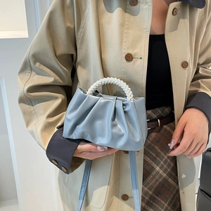 Elegant light blue pleated cloud bag with pearl handle held by a model in a beige coat