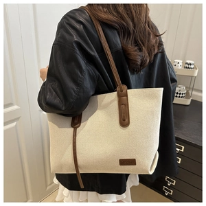 Detail of canvas tote bag showing fashion leather patch and contrast brown shoulder strap