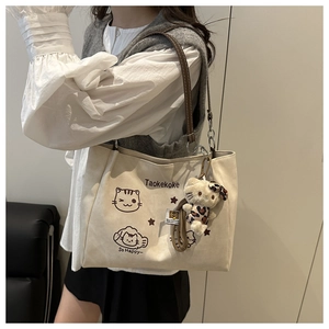Detail of a beige tote bag with cartoon cat print and plush charm shown on a model
