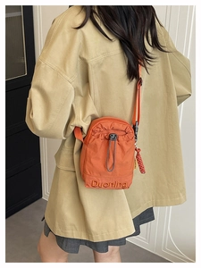 Détail d'un sac bandoulière orange avec broderie porté sur une veste beige clair